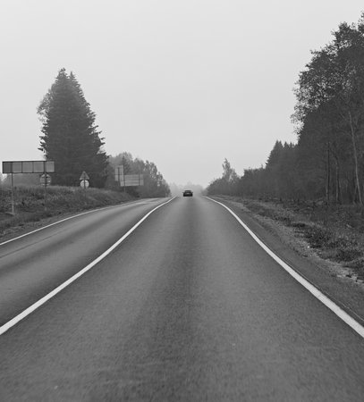 Long rural highway with a single car fading into fog, smooth asphalt, and clear markings. Sense of journey, safe driving, and freedom of travel. Horizontal orientation.の写真素材