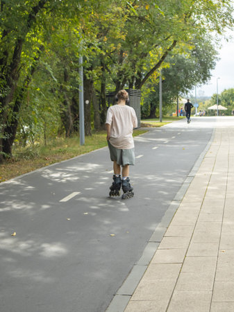 Inline skater with headphones on a shaded park path Focus on active leisure and outdoor fitness...