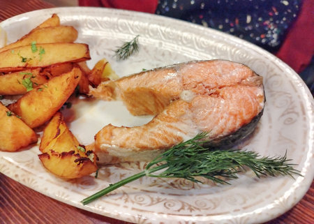 Appetizing salmon steak with crispy potato wedges and dill on ornate plate focus on fish fresh hot serving food background menu restaurant home cooking horizontal frameの写真素材