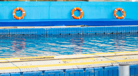 Swimming pool with bright orange lifebuoys on blue wall clean water ideal for water safety content fitness and swim training nobodyの写真素材