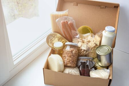 Grocery set for needy in crisis, pasta, beans, canned food etc in cardboard box on the windowsill, food donation conceptの写真素材