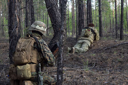 Two american soldiers are on a stakeout in the summer forest, waiting for the enemy, active military...