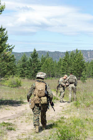 Group of fully armed american soldiers on the summer forest road on military range, active military...