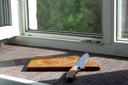 Knife and cutting board with crumbs on the windowsill, creative still life with hard light from the...