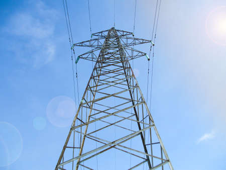 Electric power transmission lines on high voltage towers with blue sky and sun flare