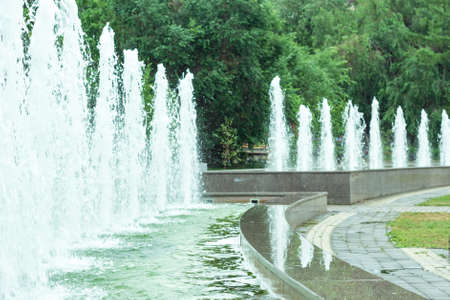 Public jet fountains in urban park area, close up of water jets and refreshing splashes over emerald water ripplesの写真素材