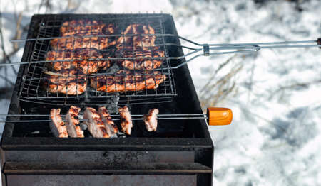 Winter barbecue outdoors, grill steak and fork with meat over hot coals in a BBQ at campside...