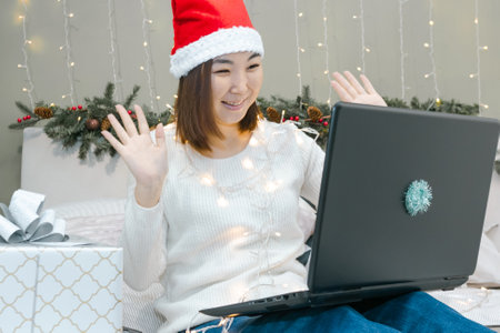 Young asian woman in santa hat say hello on laptop by video call, modern technology at New Year holiday or Christmas timeの写真素材
