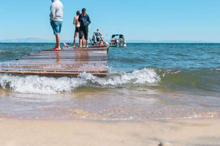 Seascape on lake, people on simple pier on coastline washed by waves, water activities, summer beach...