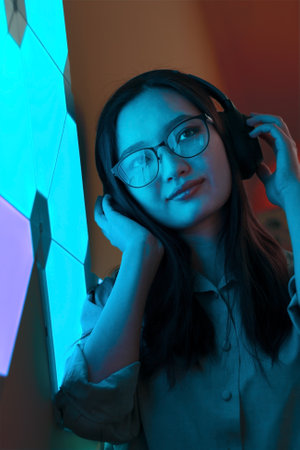 Smiling woman with headphones in violet blue neon light listen to music, nightclub futuristic neon...