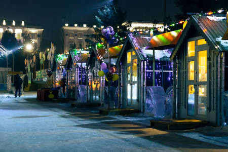Open christmas street market with small shop houses decorating with festive lights, traditional local xmas bazaar on city square illuminated with blue light at december winter nightの写真素材