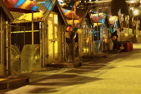 Open christmas street market with small shop houses decorating with festive lights, traditional local xmas bazaar on city square illuminated with yellow light at december winter nightの写真素材