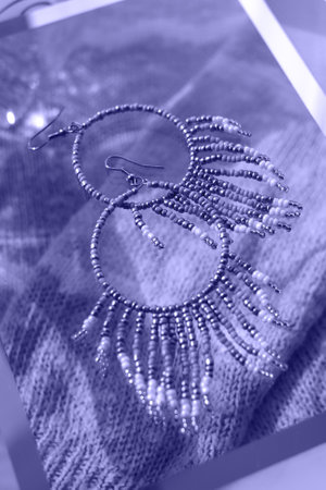 Boho jewelery earrings on glass with hard light and knit backdrop with shadows, summer accessory, vertical image in violet purple lilac tones, concept of color 2022 very periの写真素材