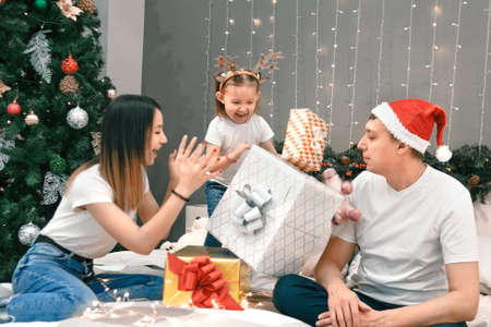 Cozy family christmas, father mother and child girl daughter play and have fun on bed with gifts, happy cheerful xmas holiday together, authentic festive lifestyleの写真素材