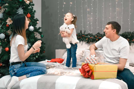 Cozy family christmas, father mother and child girl daughter play and have fun on bed with gifts, happy cheerful xmas holiday together, authentic festive lifestyleの写真素材