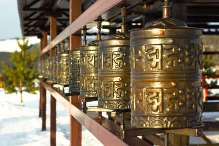 Rows of traditional copper-metal spinning prayer wheels with tibetan holy sacred mantras at snowy...