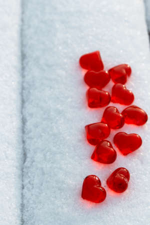 Closeup set of small bright red glass hearts on powdery snow of bench at cold winter day, symbol of...