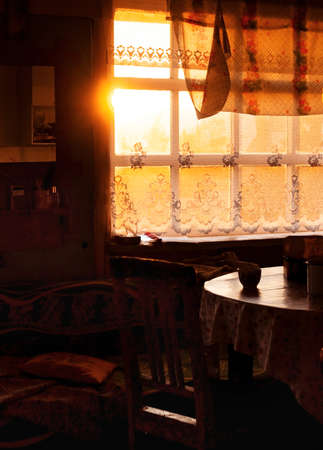 Dining room of veranda in summer house in sunset, country home of countryside in golden hour, cozy still life of rustic mood with light backlight from window and dark shadows of twilightの写真素材