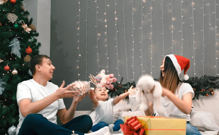 Cozy family christmas, father mother and child girl daughter play and have fun with gifts in bedroom, happy cheerful xmas holiday together, authentic festive lifestyle, gray interiorの写真素材