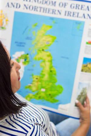 Woman looks at poster map of England, English teacher with educational training material on foreign language, top view, vertical imageの写真素材
