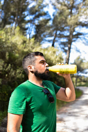 Young man taking a break from hiking and drinking water of a yellow bottleの写真素材