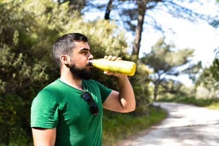 Young man taking a break from hiking and drinking water of a yellow bottleの写真素材