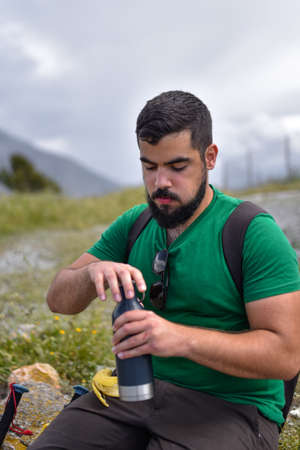 Man opening a blue bottle during a break from a hiking dayの写真素材