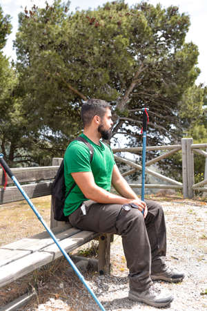 Young man taking a break from hiking sitting in a bankの写真素材