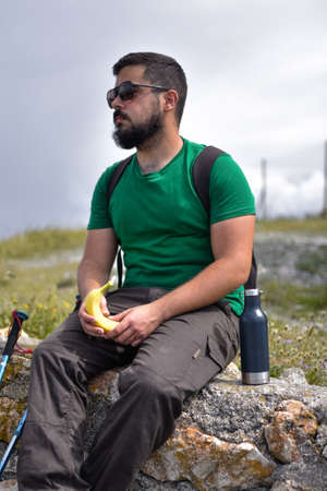 Young man with sunglasses taking a break and eating a banana and a energetic drink while he is sittingの写真素材