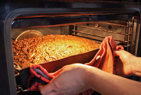 Baker hands with potholder next to metal cookie sheet with bread in ovenの写真素材