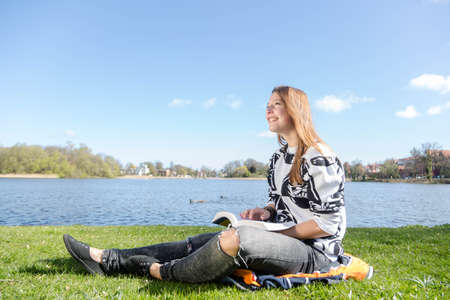 A woman reads a book in a park during nice weatherの写真素材