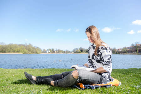 A woman reads a book in a park during warm weatherの写真素材