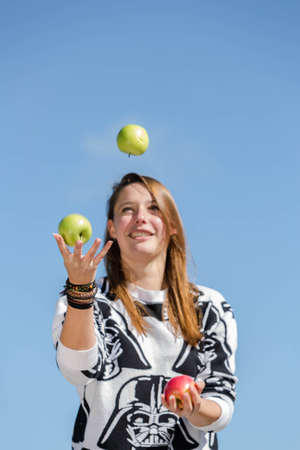 A young woman smiles and juggling with three crunchy and healthy applesの写真素材