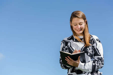 Young smiling woman making herself up during nice weather and ideas recorded in a small bookの写真素材