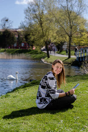 Young woman sitting at a lake with a tablet and laughing into the cameraの写真素材