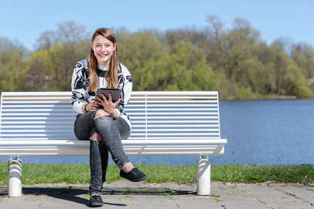 Young woman sitting on a bench in a park with a new tablet and laughing into the cameraの写真素材