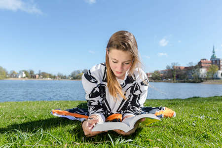 A young woman reading lying in a park a book in the sunの写真素材