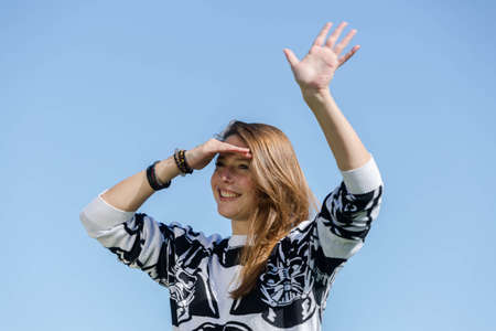 Laughing young woman recognizes her friends and waves them with one handの写真素材