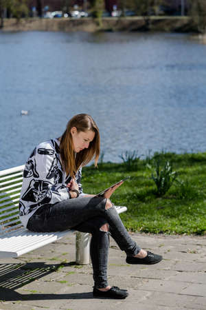 Young woman sitting on a beautiful day in the park on a bench with a Tabletの写真素材
