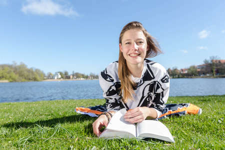 A young woman lies at a lake and laughs into the camera during nice weatherの写真素材