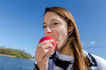 A woman eating a red apple with many vitamins outdoorの写真素材