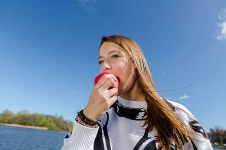 A young woman biting into a red apple and looking at the cameraの写真素材