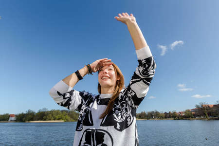 Young woman meets her friends in a park and waves them with a hand full of anticipationの写真素材