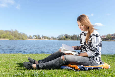 Young woman reading and skimming through a book during nice weather in a parkの写真素材