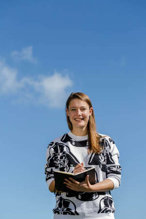 Young student is thinking and taking notes in a small book during nice weatherの写真素材