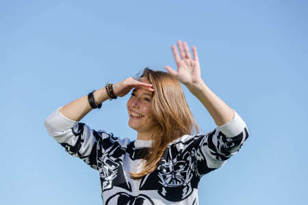 Laughing young woman recognizes her friends and waves them with one handの写真素材