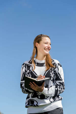 Young smiling woman making herself up during nice weather and ideas recorded in a small bookの写真素材