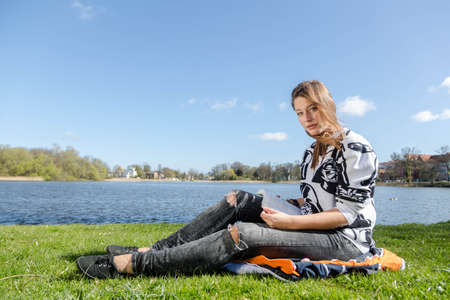 A woman reads a book in a park during nice weatherの写真素材