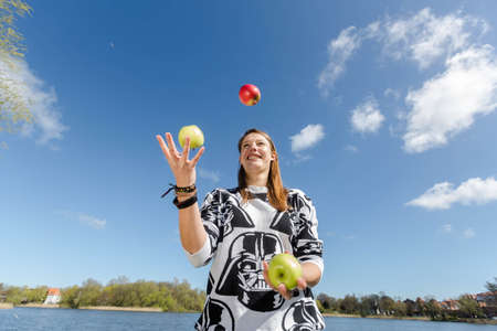 A slender young woman juggling with three crunchy applesの写真素材