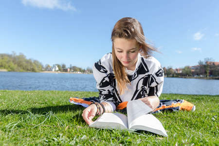 Student skimming through a book at a lake in the sunshineの写真素材